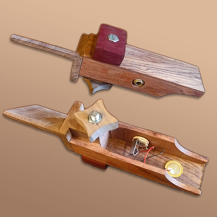 Picture of table clamp daxophone. The top part of the image shows a daxophone in the playing position. The left part of the daxophone is cut to the shape of a thin flat piece of wood that is 45-degrees off axis. The body features a clamp piece consisting of a rectangle on top connecting through the body via a bolt to a wooden knob on the bottom. The bottom part of the image reveals that the daxophone was constructed by attaching two side panels to the block on the back where the clamp goes through. A quarter-inch jack is embedded in one of the side panels. It is connected to a piezo element that is attached to the underside of the flat top plate.